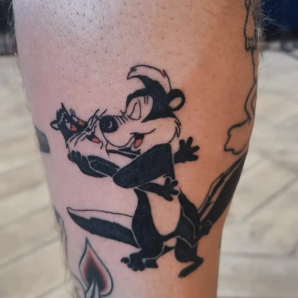 Full-color Pepe Le Pew and Penelope chase-scene tattoo on the outer leg