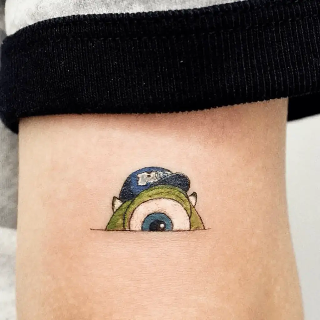 Minimalist Mike Wazowski eye tattoo with green and blue ink